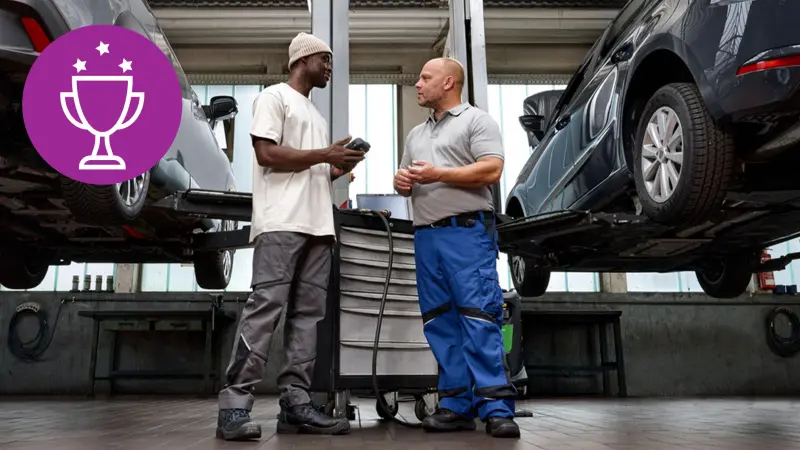 Werkstattmitarbeiter und Trainer in moderner Bosch-Werkstatt zwischen Fahrzeugen auf Hebebühnen – Training für Fahrzeugtechnik