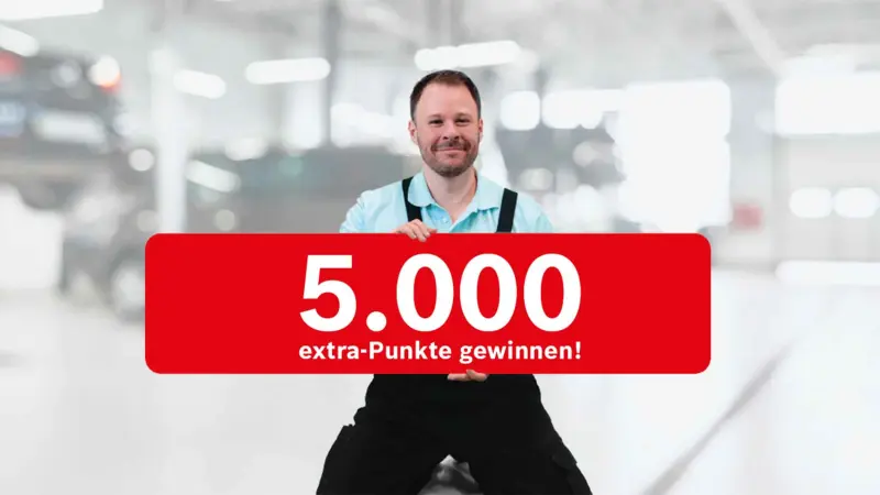 Schild mit Hinweis "5.000 extra-Punkte gewinnen!" wird von Mechaniker in einer Werkstatt präsentiert.
